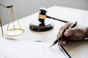 Attorney at work, on the table there is a small hammer to beat the judges table in court. and justice scales, lawyers are drafting a contract for the client to use with the defendant to sign.